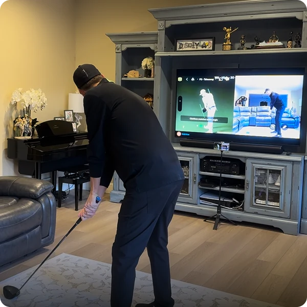 A golfer practising indoors, mirroring his swing to the television